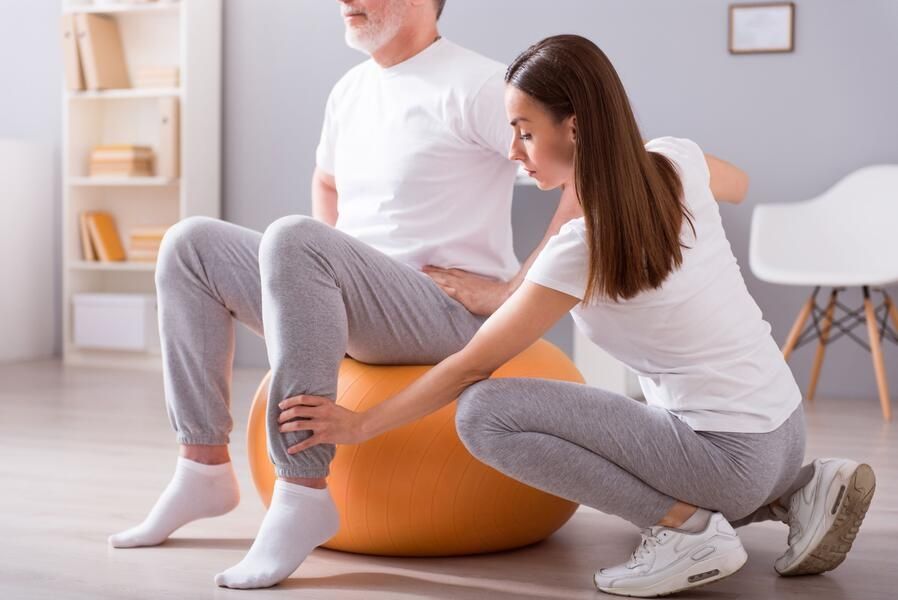 Therapeutin unterstützt einen Patienten beim Training mit dem Gymnastikball